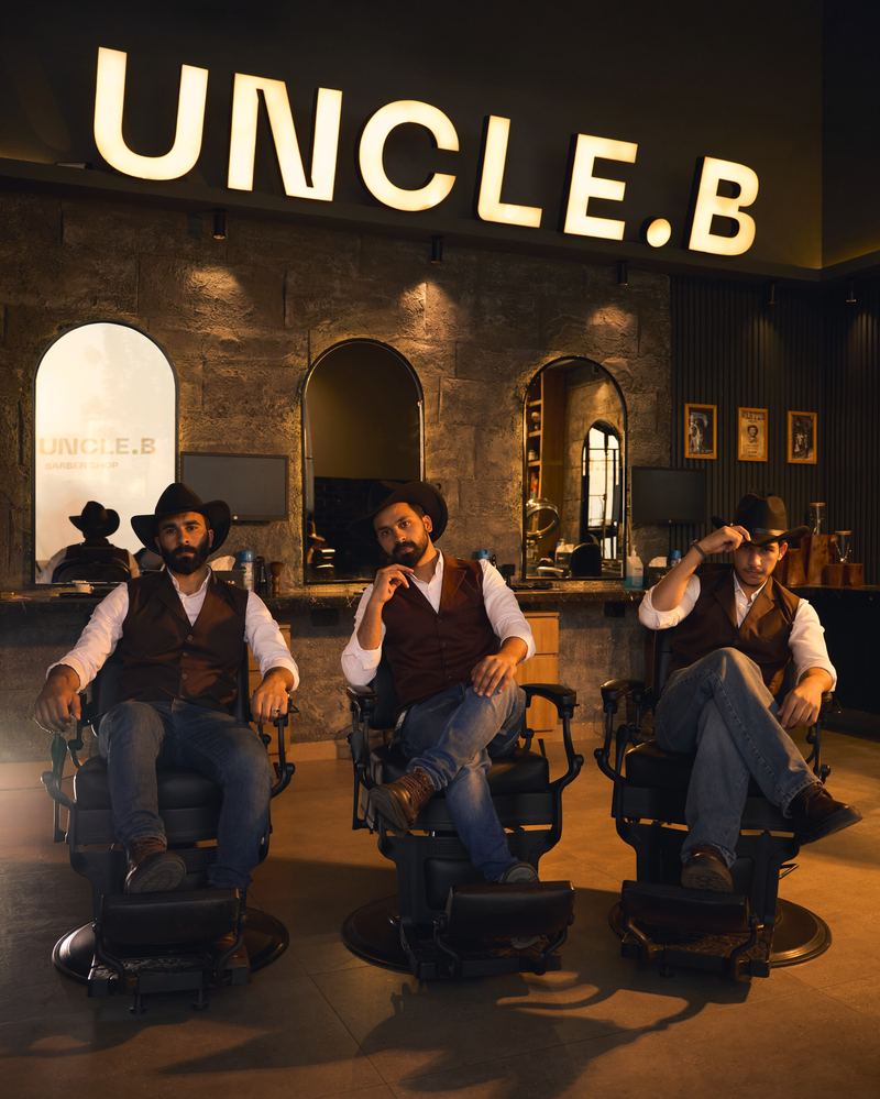 The Uncle B barbers in cowboy hats and vests, seated in barber chairs